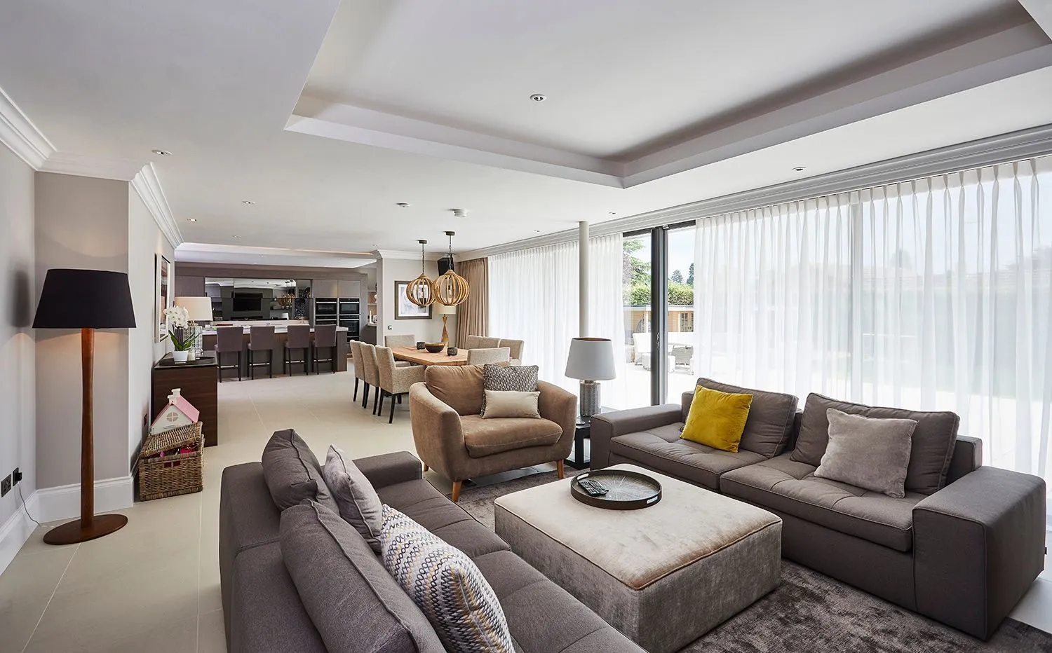 Open-plan lounge with grey sofas, a floor lamp and sheer curtains