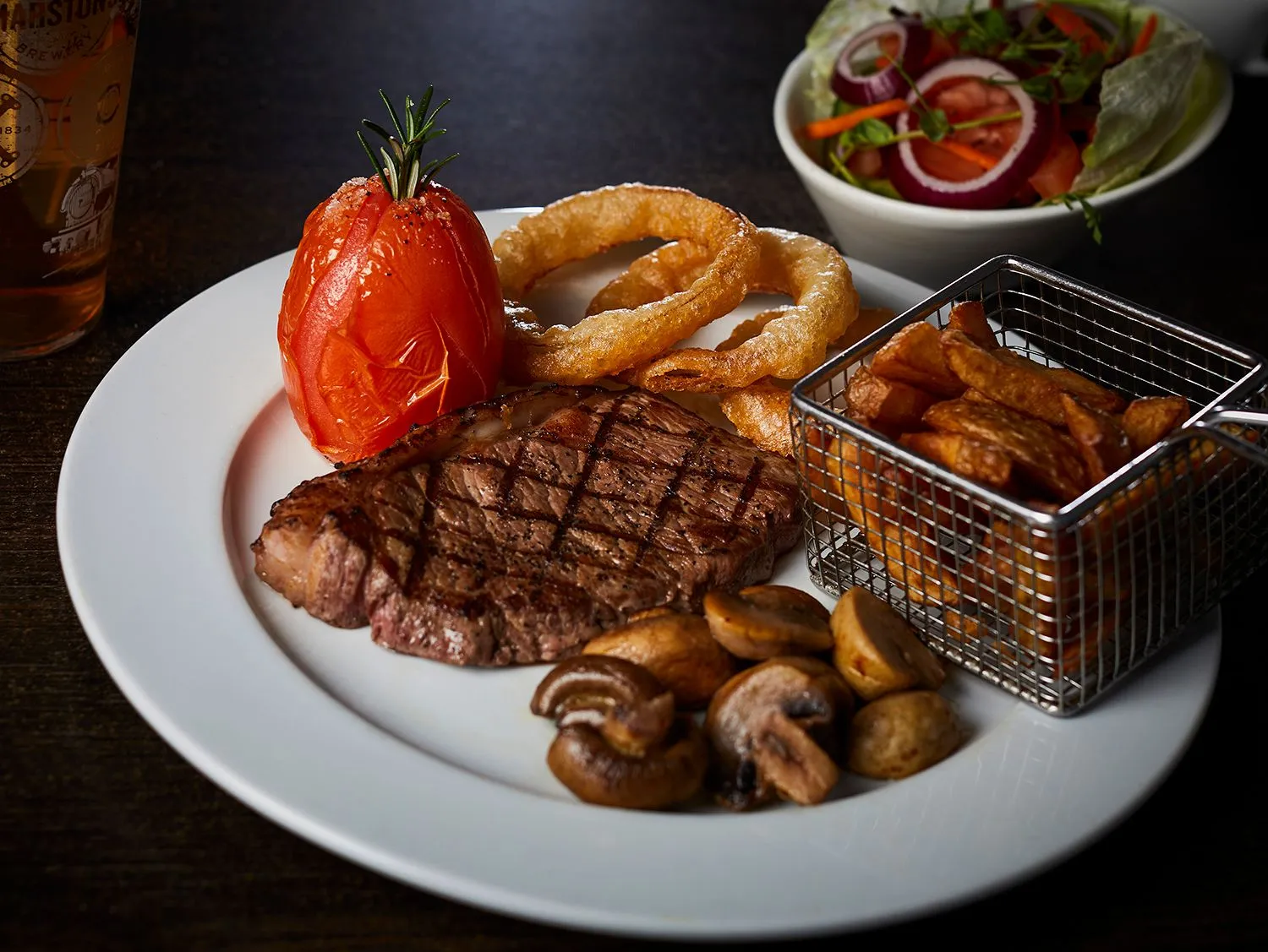 Grilled steak with a roasted tomato, onion rings and mushrooms