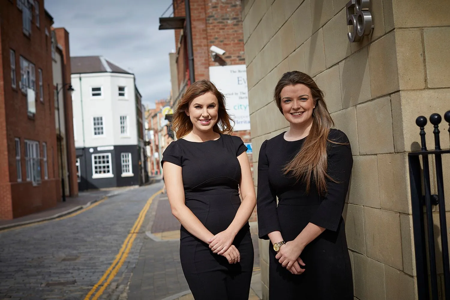 Two women in black dresses standing on a cobbled street