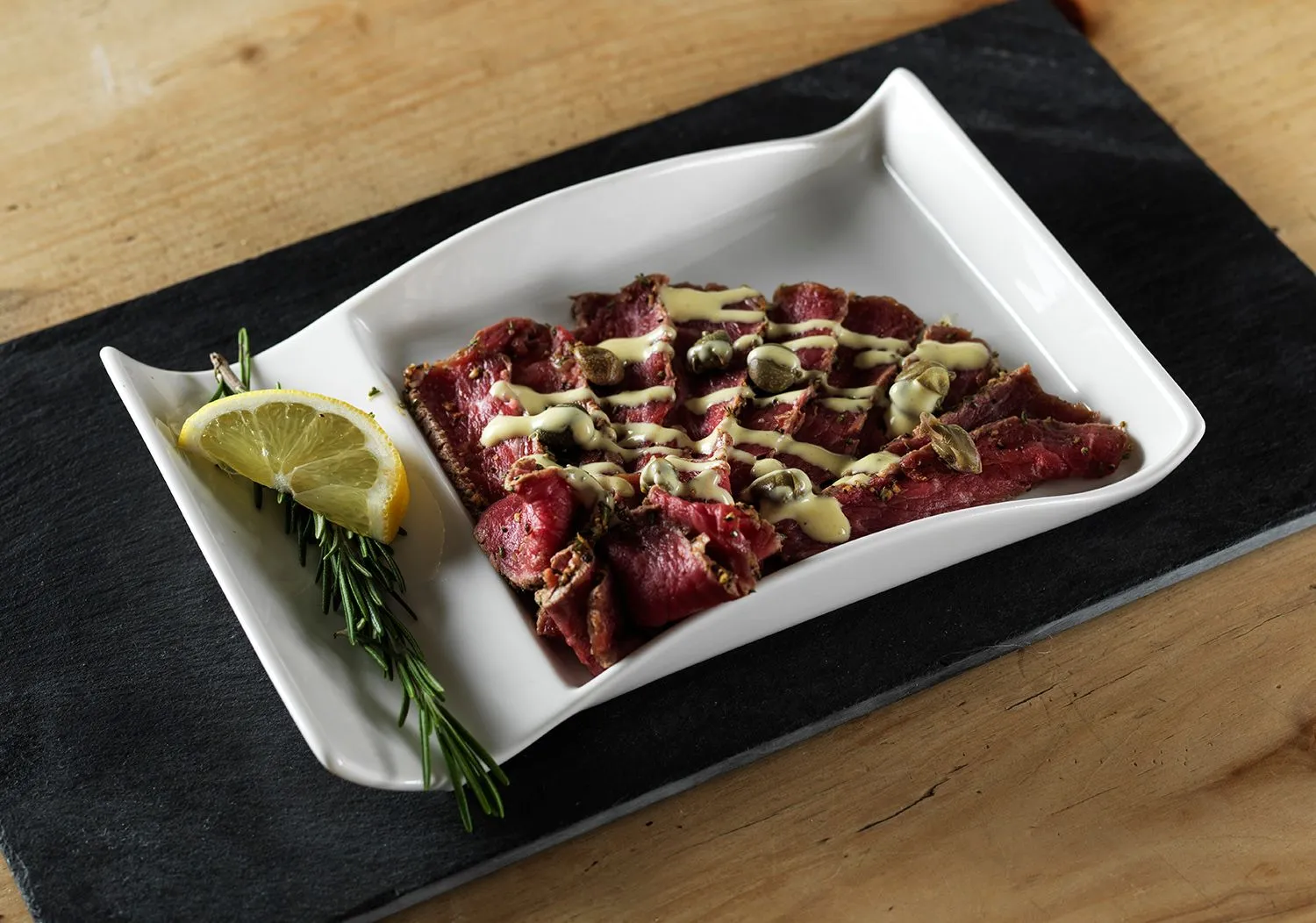 Beef carpaccio on a white plate with lemon and rosemary