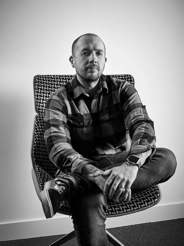 Black and white portrait of Nick Freeman sitting cross-legged in a patterned lounge chair