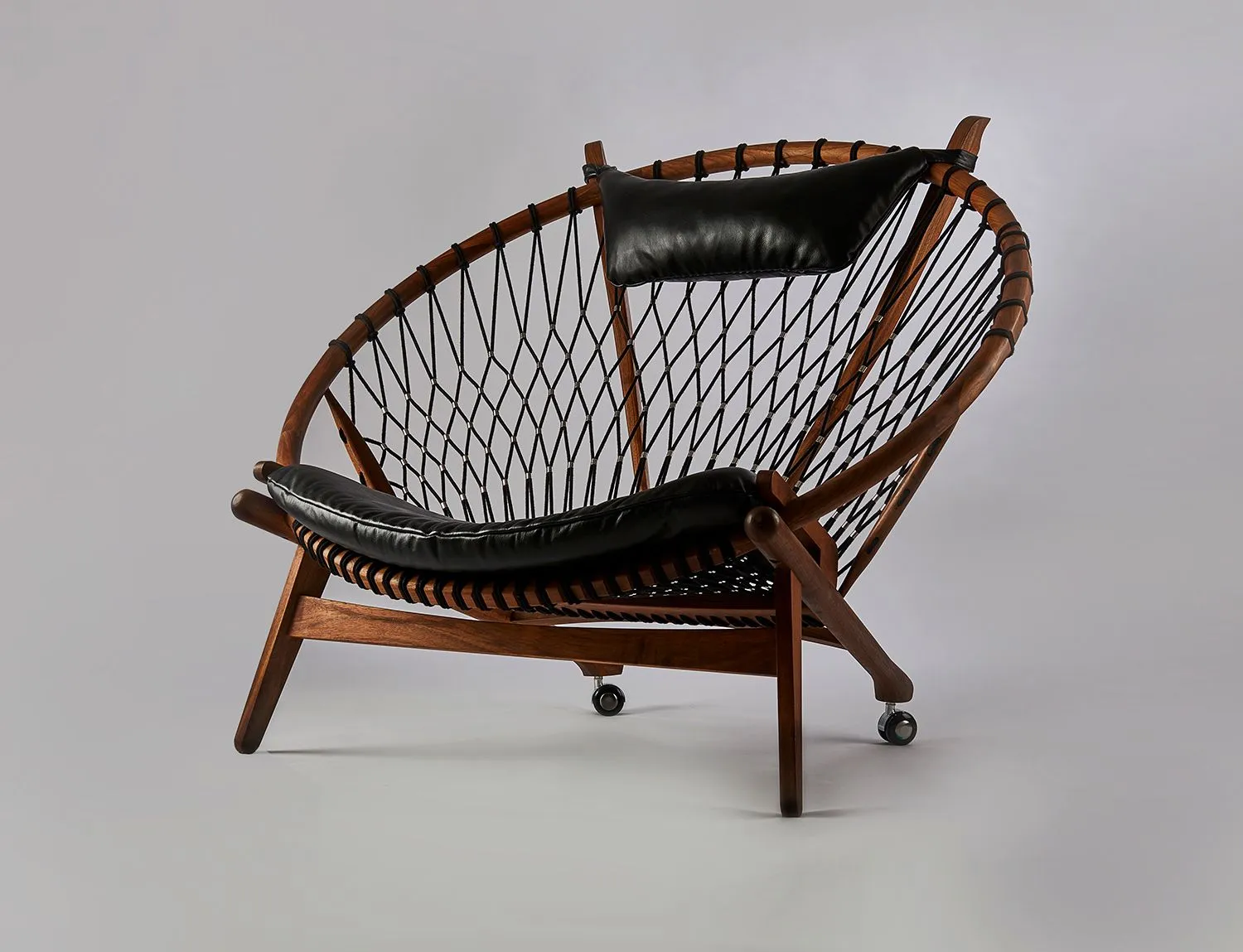 Hoop chair with a timber frame, rope weave and black leather cushions on a grey seamless backdrop