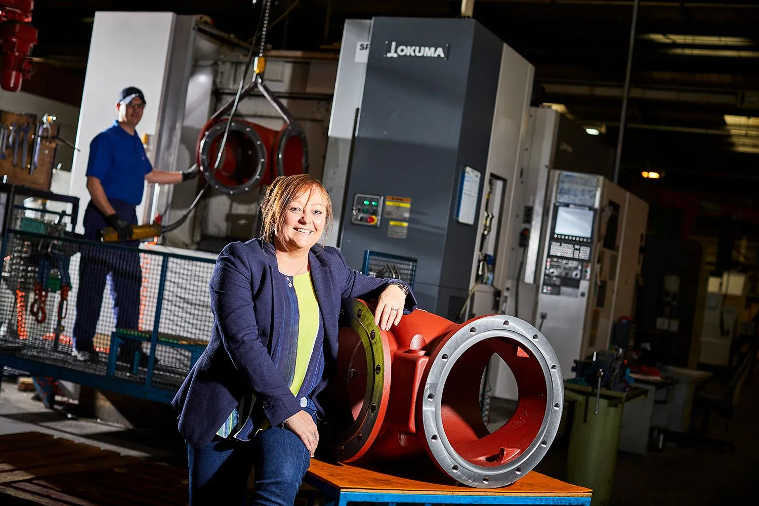 Woman in a blazer seated beside machinery in an engineering workshop