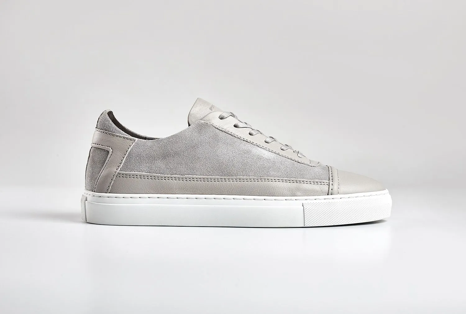 Grey suede trainer photographed side-on against pure white