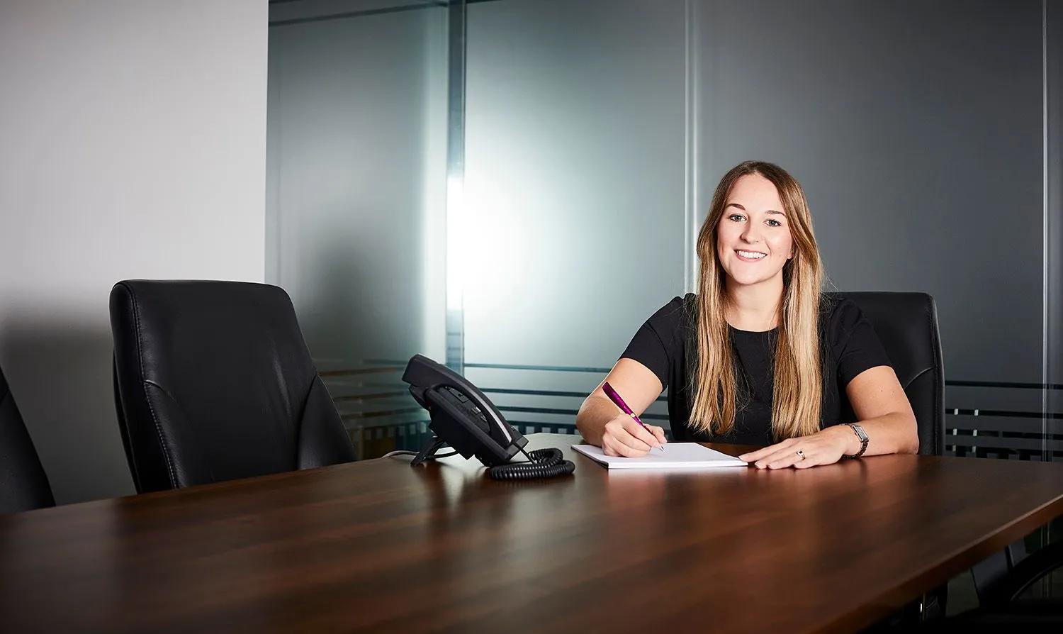 Smiling woman writing at a boardroom table