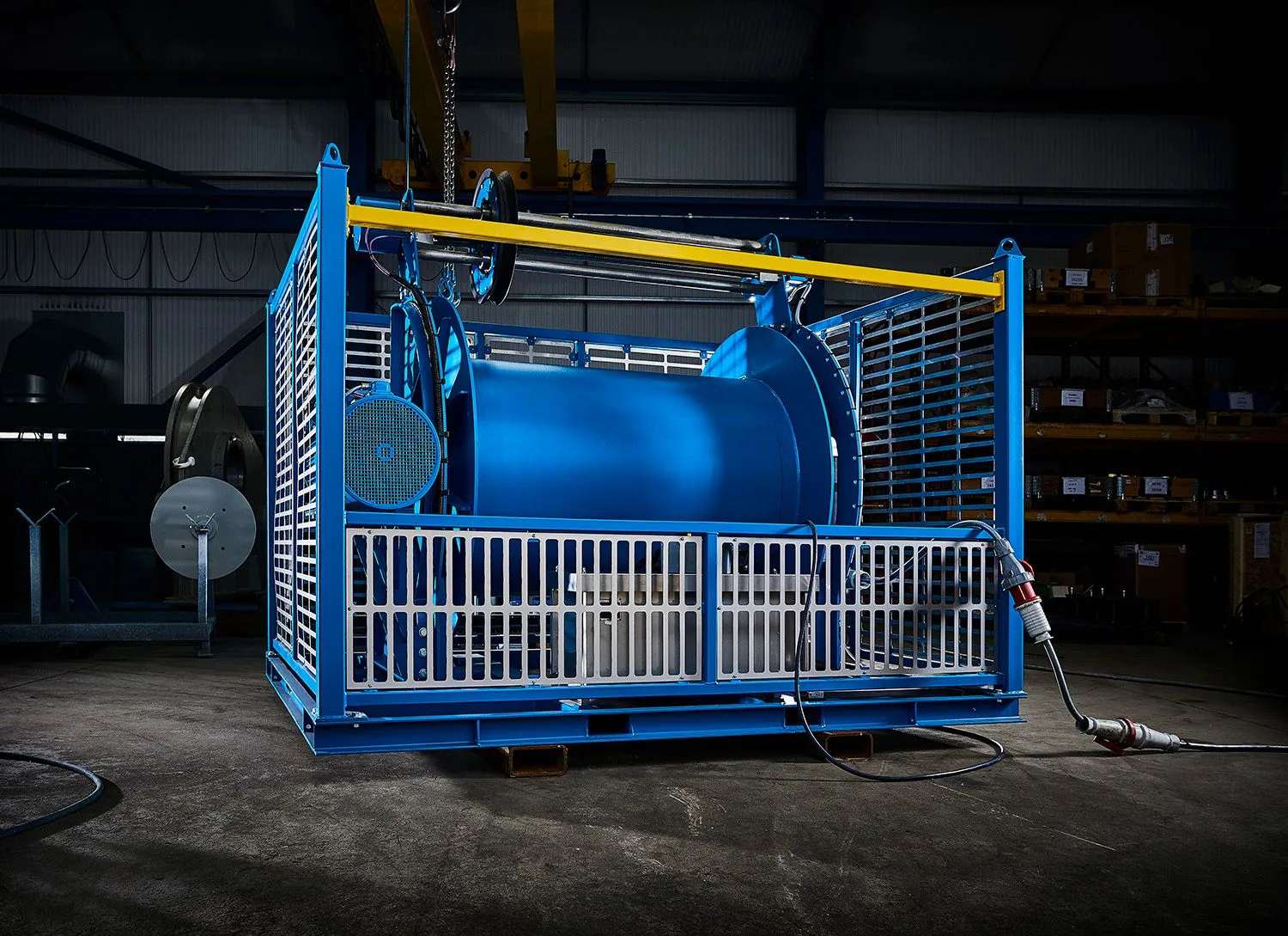 Blue industrial winch in a caged steel frame on a factory floor