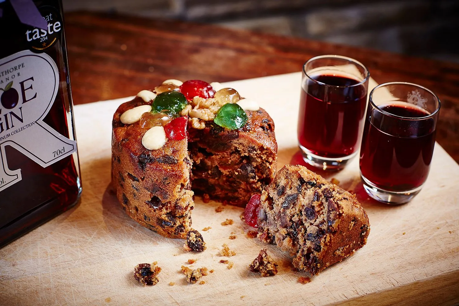 Fruit cake topped with glacé cherries beside two glasses of sloe gin