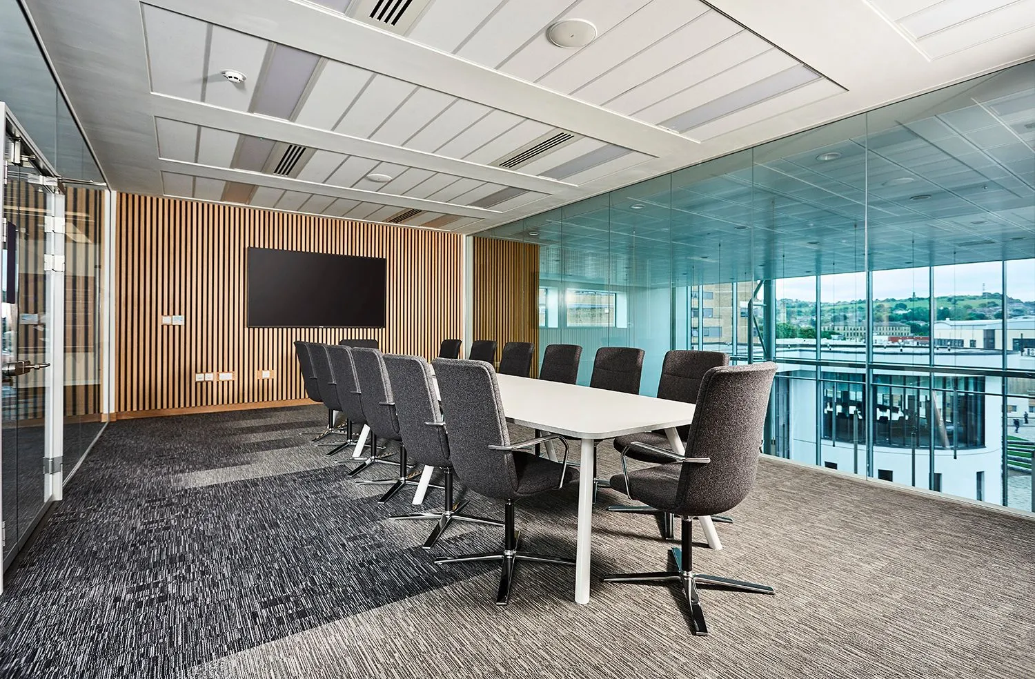 Boardroom with a long white table, grey chairs, timber slatted wall and floor-to-ceiling glass