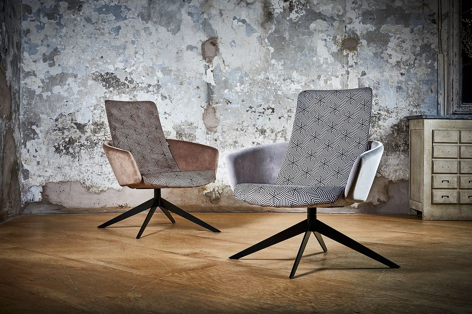 Two upholstered swivel chairs on a wooden floor against a distressed plaster wall