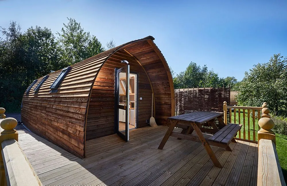 Timber glamping pod with a decked terrace under blue sky