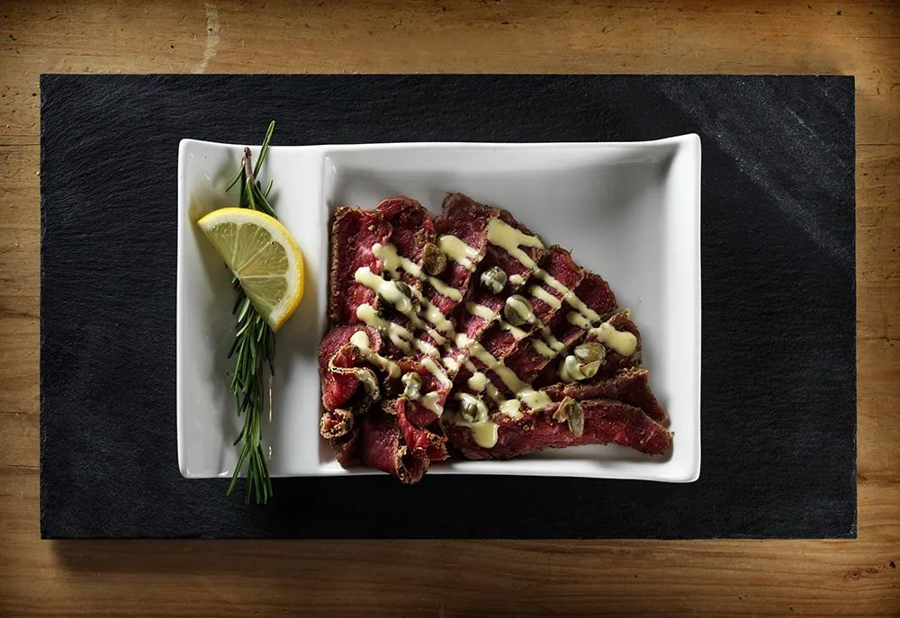 Beef carpaccio plated on slate with lemon and rosemary