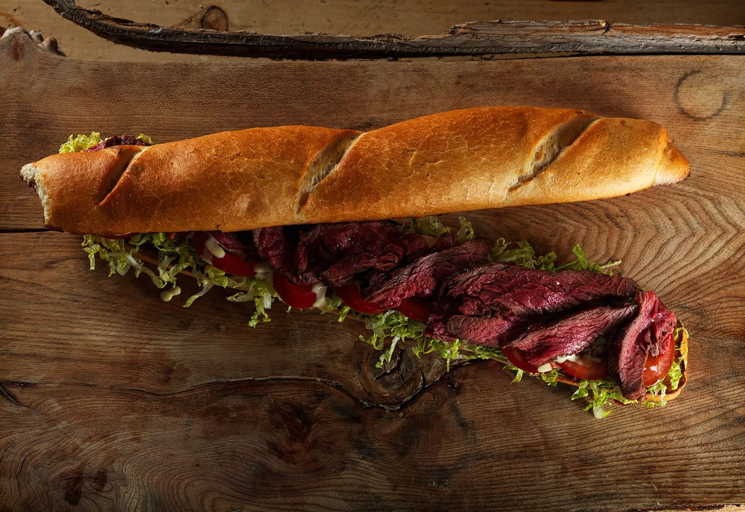 Rare steak baguette with frisée on a rustic board