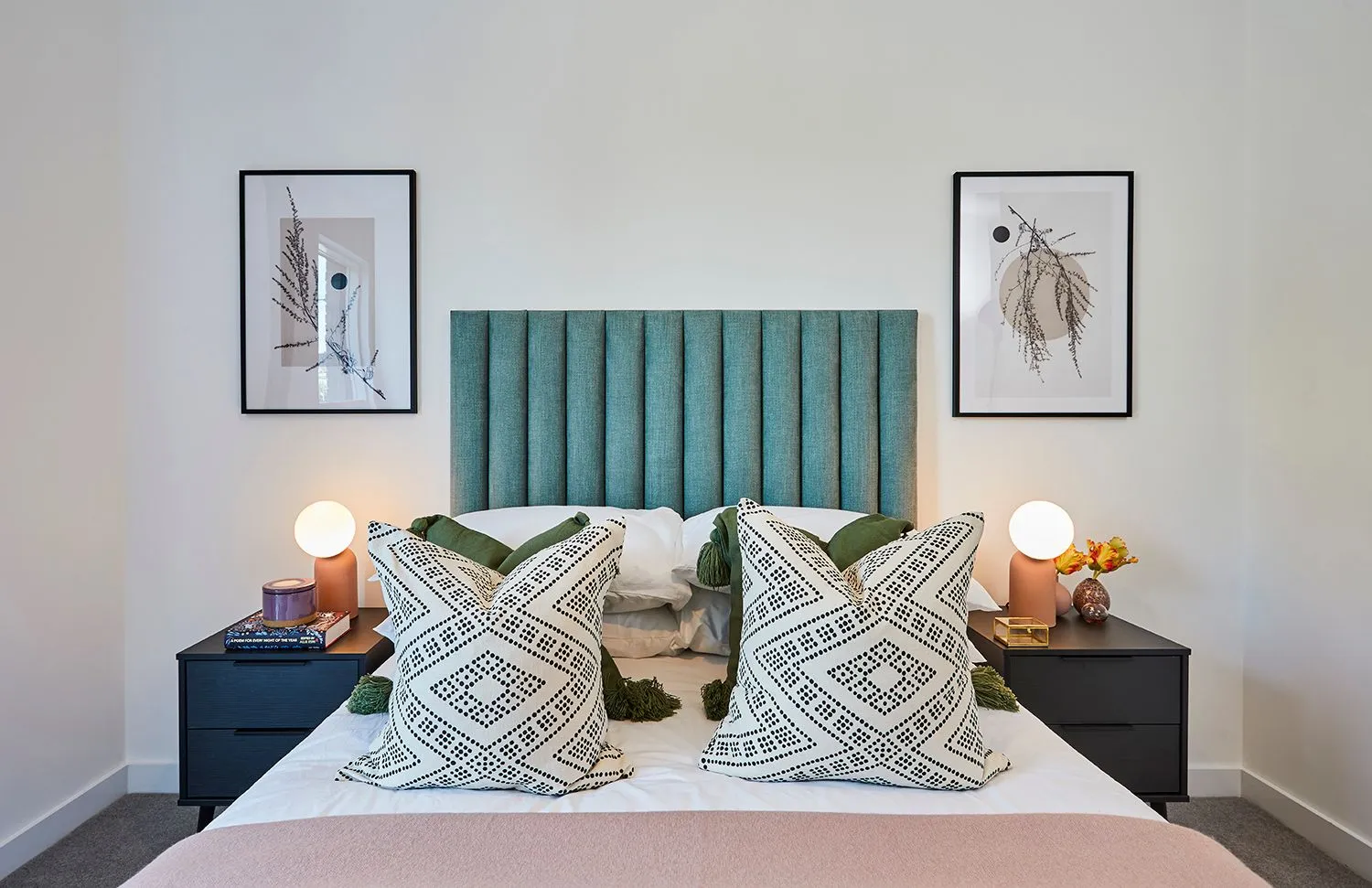 Bedroom with a teal headboard, patterned cushions and framed prints
