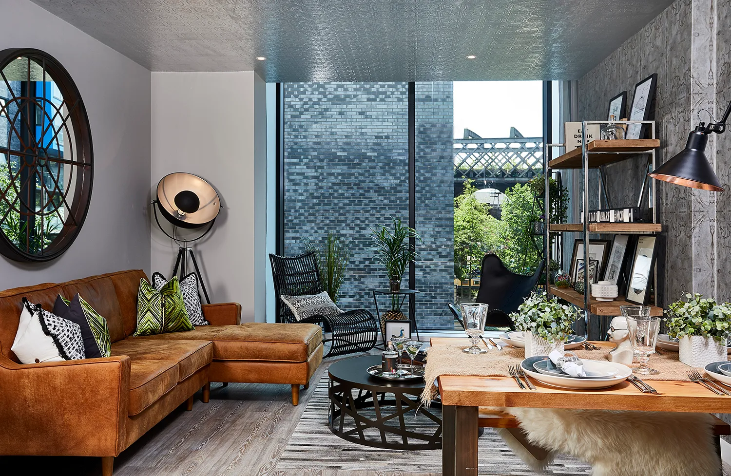 Open-plan living and dining space with a tan leather sofa and glass doors to a planted terrace